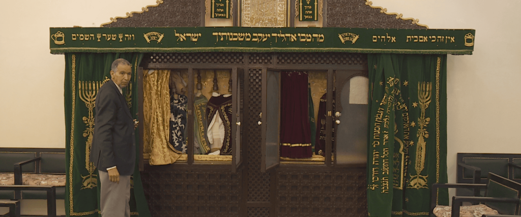 Image du film Ziyara d'un marocain musulman à côté d'une armoire où il y a des Sefer Torah